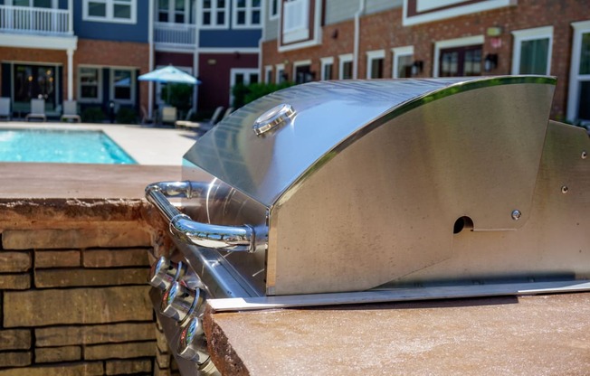 a grill sitting on top of a brick wall near a pool