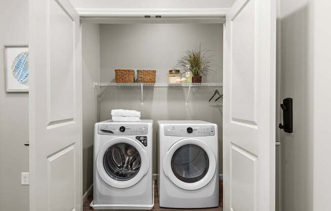 A white laundry room with two washing machines and a shelf above them.
