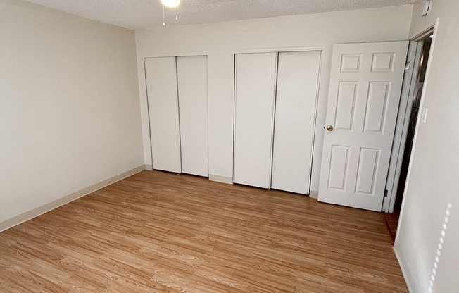 Bright and airy bedroom with elegant wooden flooring and ample closet space, perfect for a cozy living environment.