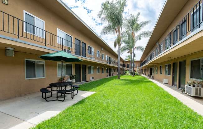 A grassy area in front of apartment buildings with a picnic table and umbrella.