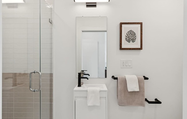 A white bathroom with a glass shower stall and a white sink vanity.
