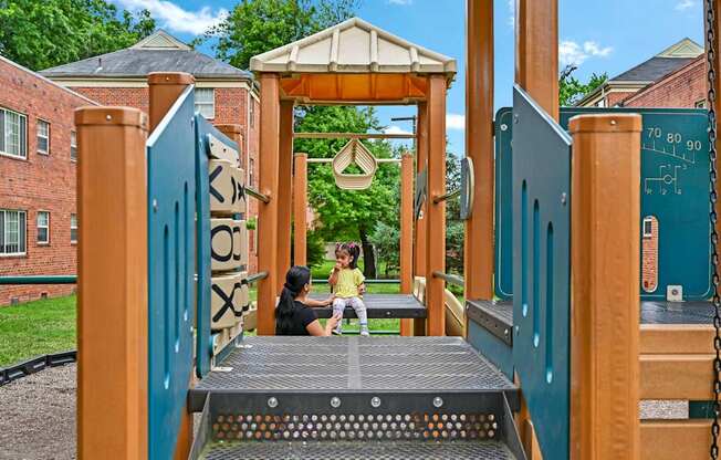 a woman and a child sitting on a swing on a playground at Hamilton Manor Apartments, Hyattsville