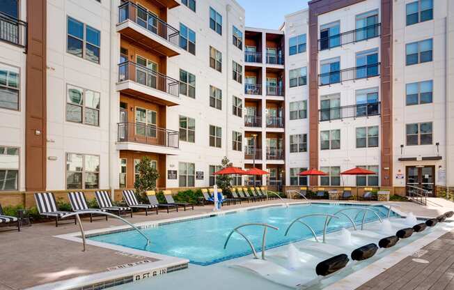 a swimming pool with chaise lounge chairs and umbrellas in front of an apartment building