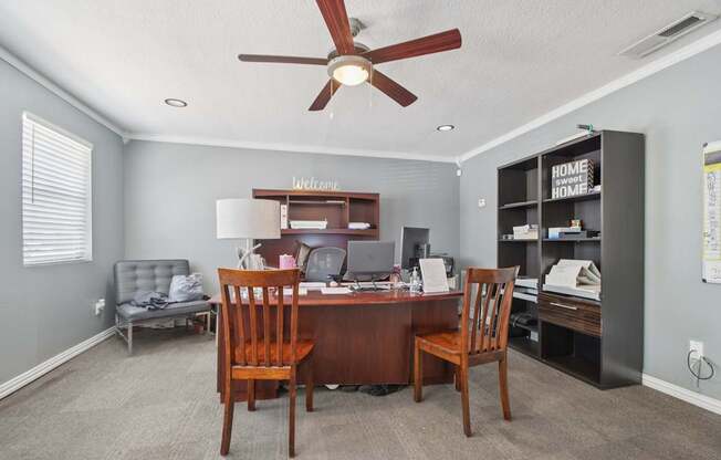 A room with a desk, chairs, and a ceiling fan.