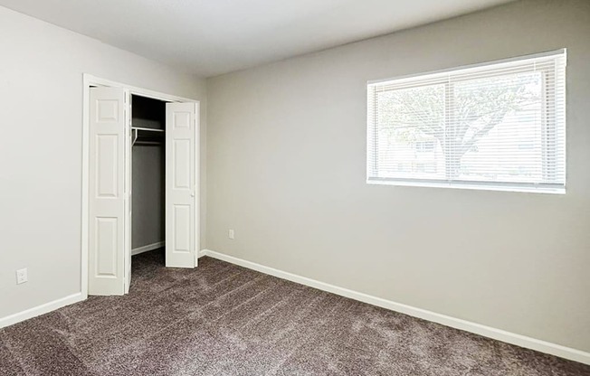 A room with a carpeted floor and a window with blinds.