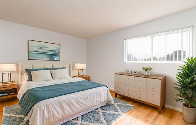 A bedroom with a bed, nightstands, and a plant.