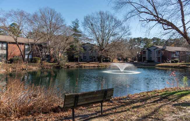 A park with a bench and a pond with a fountain.