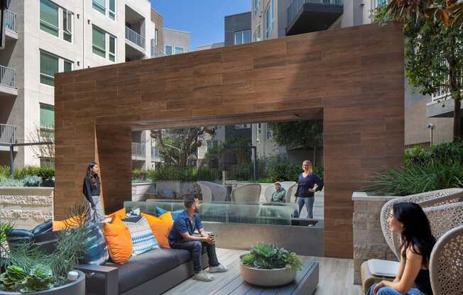 people sitting on couches and chairs on a patio with a wooden wall in the background