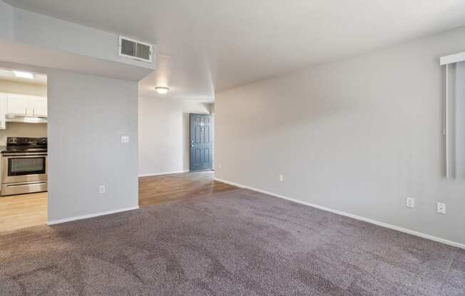 the living room and dining room of an apartment with carpeting and a kitchen