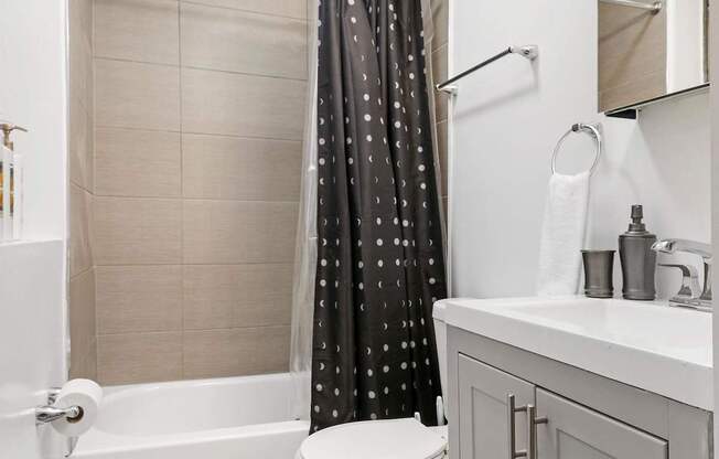A white toilet with a black shower curtain with white dots.