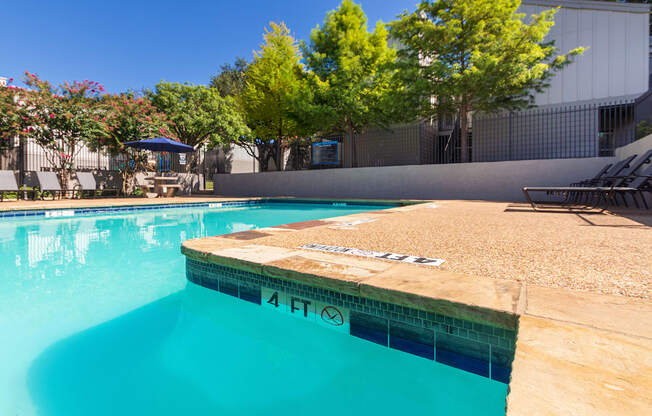 A pool surrounded by chairs and trees at The Biltmore Apartments located in the Vickery Midtown neighborhood of Dallas, TX.