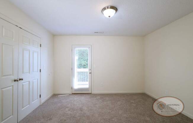 A carpeted bedroom with walk in closet and door to patio.