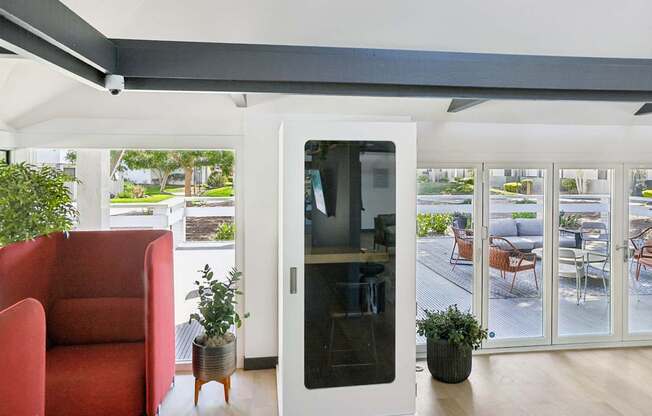 A red chair is in the foreground of a room with a glass door leading to a balcony.
