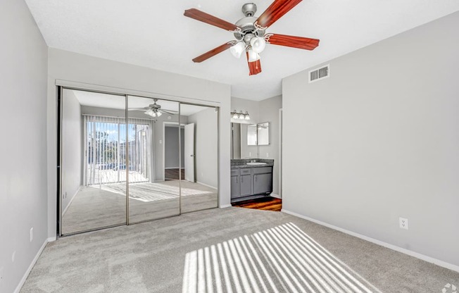 A bedroom with a ceiling fan and a closet with sliding mirrored doors at Montfort Crossing Apartments in Dallas, TX.