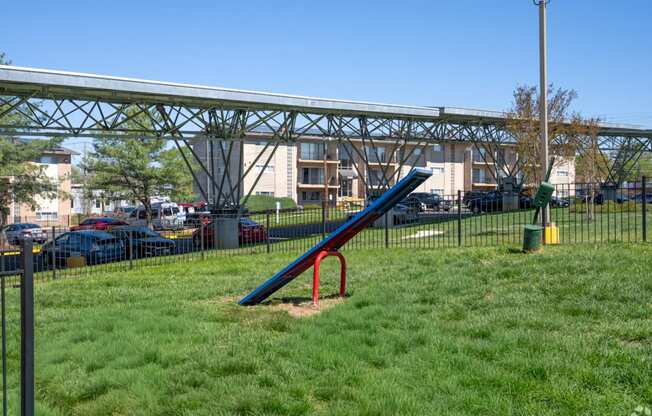 A playground with a blue and red slide in the foreground and a metal structure in the background.