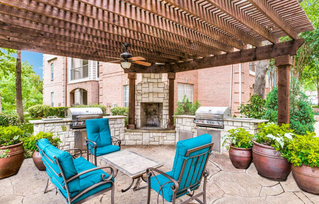 Luxury Apartments in North Dallas TX- Outdoor Patio With Fireplace, Two Grills, and Comfortable Blue Outdoor Chairs