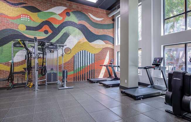 A gym with treadmills and a colorful mural on the wall.