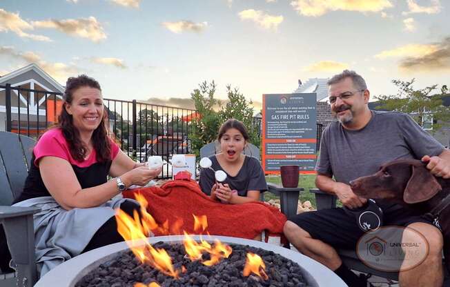 A family sitting around the fire pit with their dog, laughing and roasting marshmallows as the sun sets.