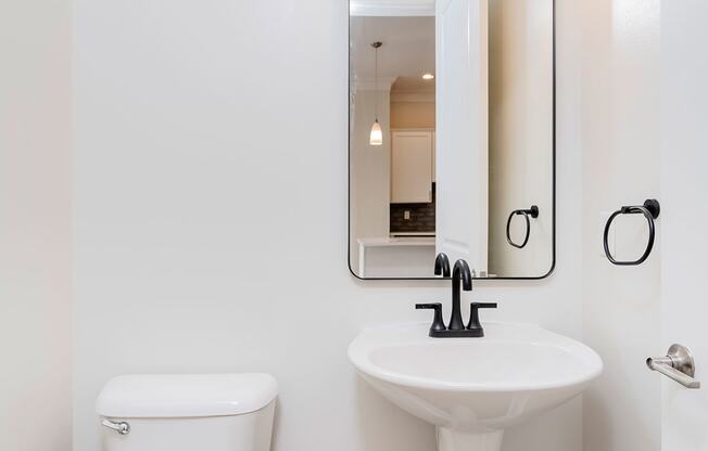 a bathroom with white walls and a white toilet next to a sink with a mirror above it