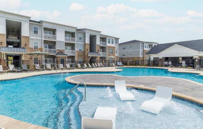 a large swimming pool with white lounge chairs in front of an apartment building