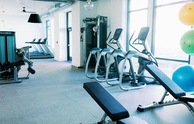 a gym with cardio equipment and large windows at The Merchant Apartments, Charleston