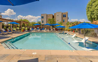 a swimming pool with blue umbrellas and chairs and a building in the background