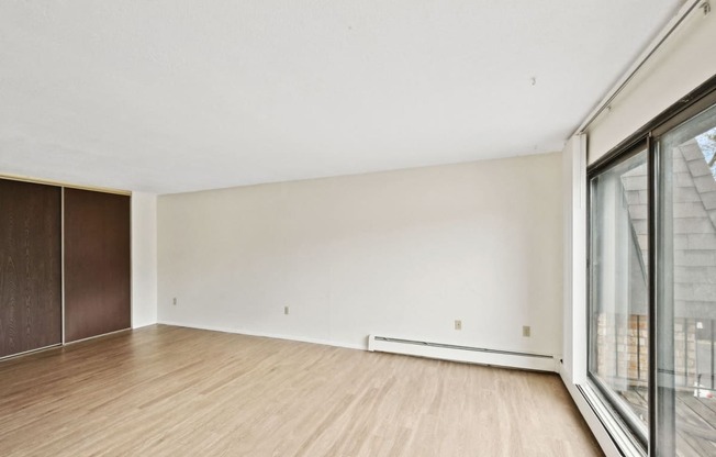 the living room of an apartment with wood flooring and large windows