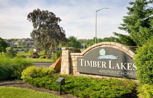 A sign for Timber Lakes Apartment Homes is displayed in front of a green lawn.