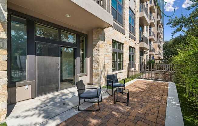 Two chairs are on a brick patio in front of a building.