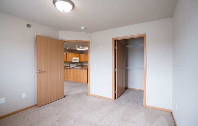 A room with a carpeted floor and a wooden door. Fargo, ND East Bridge Apartments
