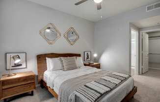 A bedroom with a bed, nightstand, and two mirrors on the wall.