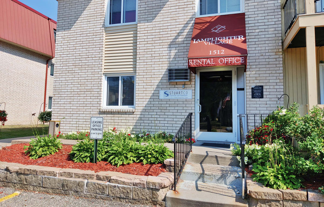 the front entrance of an apartment building with a flower bed in front of the door