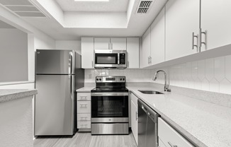 Model kitchen at our apartments in Clearwater, FL, featuring stainless steel appliances, grey counters, and white cubpboards.