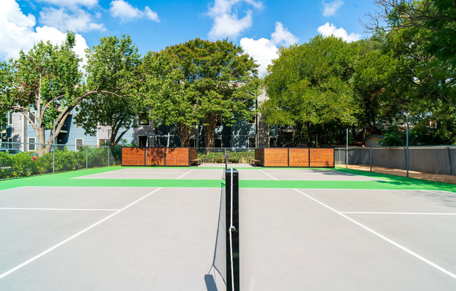 a tennis court with trees and buildings in the background