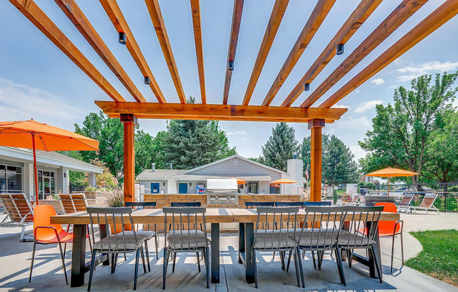 A wooden pergola with orange chairs and tables is set up for outdoor dining.