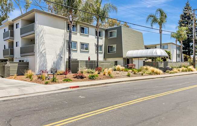 A street view of a residential area with apartment buildings and palm trees.
