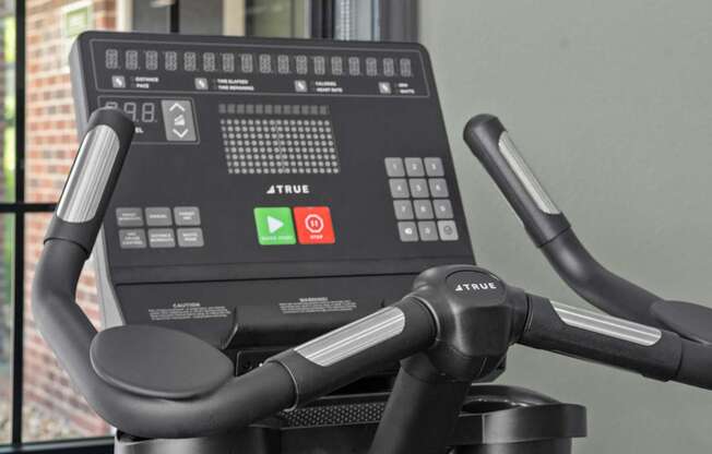 A close up of a True bike workout machine with a digital screen and handlebars.