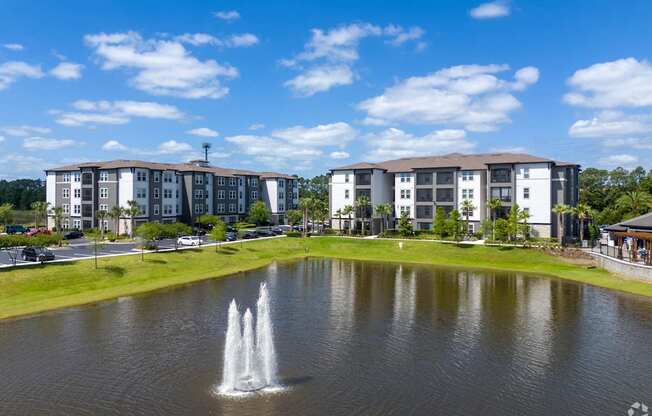 A fountain in the middle of a pond in front of apartment buildings.