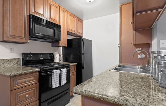 Studio apartments in Mar Vista CA - Vista - Kitchen with Sandy Granite Countertops, Wooden Cabinetry, Microwave, Oven, Stove, and Refrigerator, and Dual Sink