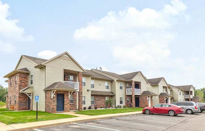 A red car is parked in a parking lot in front of apartment buildings.