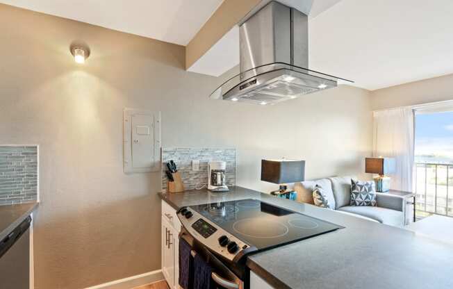 Kitchen with stainless steel electric range over range hood, gray quartz counters, wood-style floors