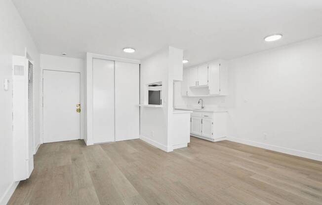 an empty living room and kitchen with white walls and wood flooring