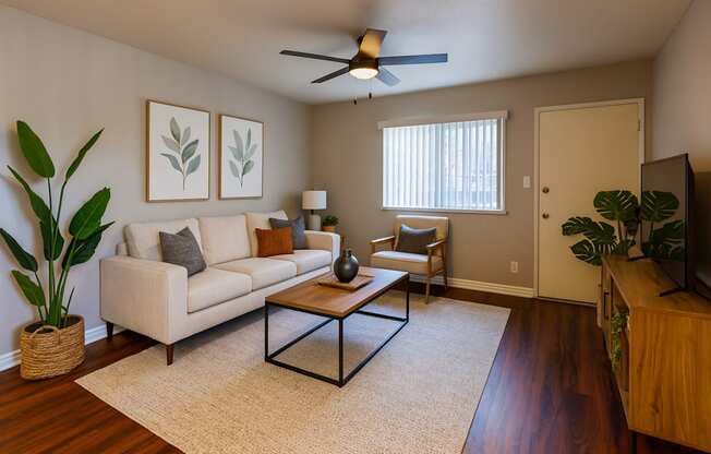 A living room with a beige couch, a coffee table, and a ceiling fan.