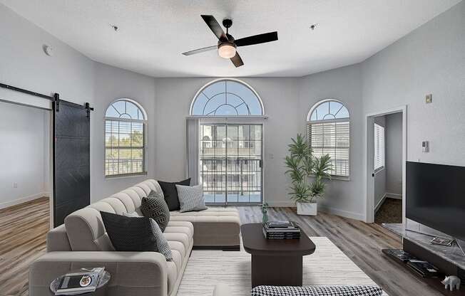 A living room with a grey sofa, a coffee table, a ceiling fan, and a sliding glass door.