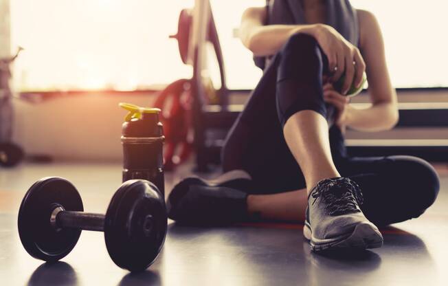 a woman sitting on the floor next to a dumbbell and a drink