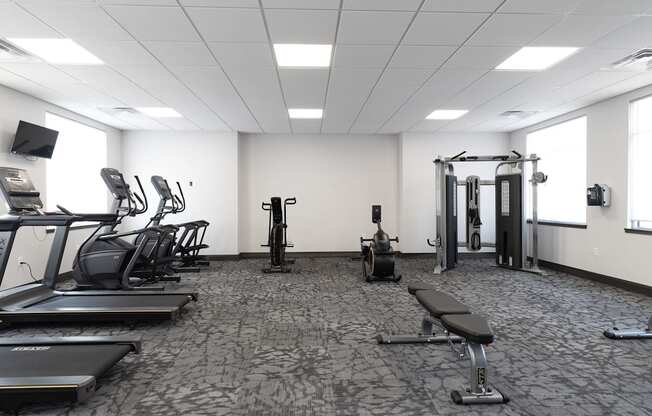 a gym with cardio equipment and weights in a room with windows