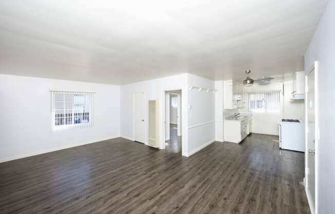 an empty living room and kitchen with white walls and wood floors