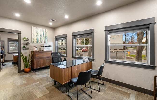 A room with a desk and chairs in front of a window with a view of a street.