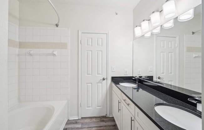 Bathroom with double sinks, black countertop, white shower and tub.