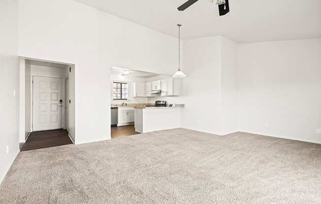 A large, empty dining and living room with a carpeted floor and a kitchen area in the background at Tanglewood Apartments, Oak Creek, WI